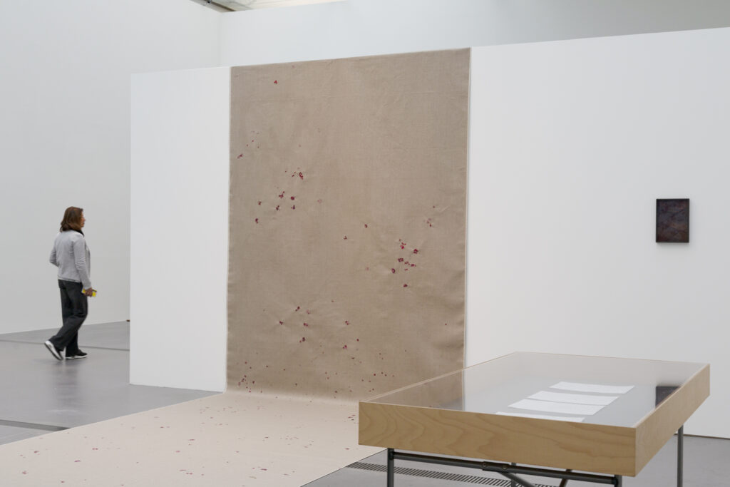 Ausstellungsansicht der Ausstellung "Vertical Horizon" im Lentos Kunstmuseum Linz, im Rahmen der Kyiv Biennale 2025. Zu sehen ist die Arbeit "wie eine Geranie rot" der aus der Ukraine stammenden bildenden Künstlerin Elena Kristofor. Eine Leinwand mit Abdrücken der Geranienblüten, eine Vitrine mit Drohnen-Gedichten verfasst von KI